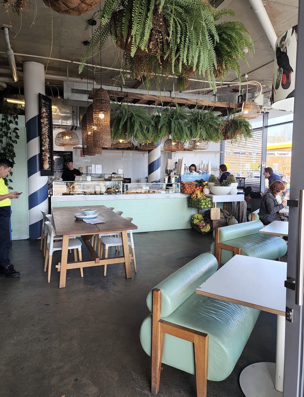 Inside Lexpressohouse with mint booth seating, hanging ferns, wicker lights and a pastry counter